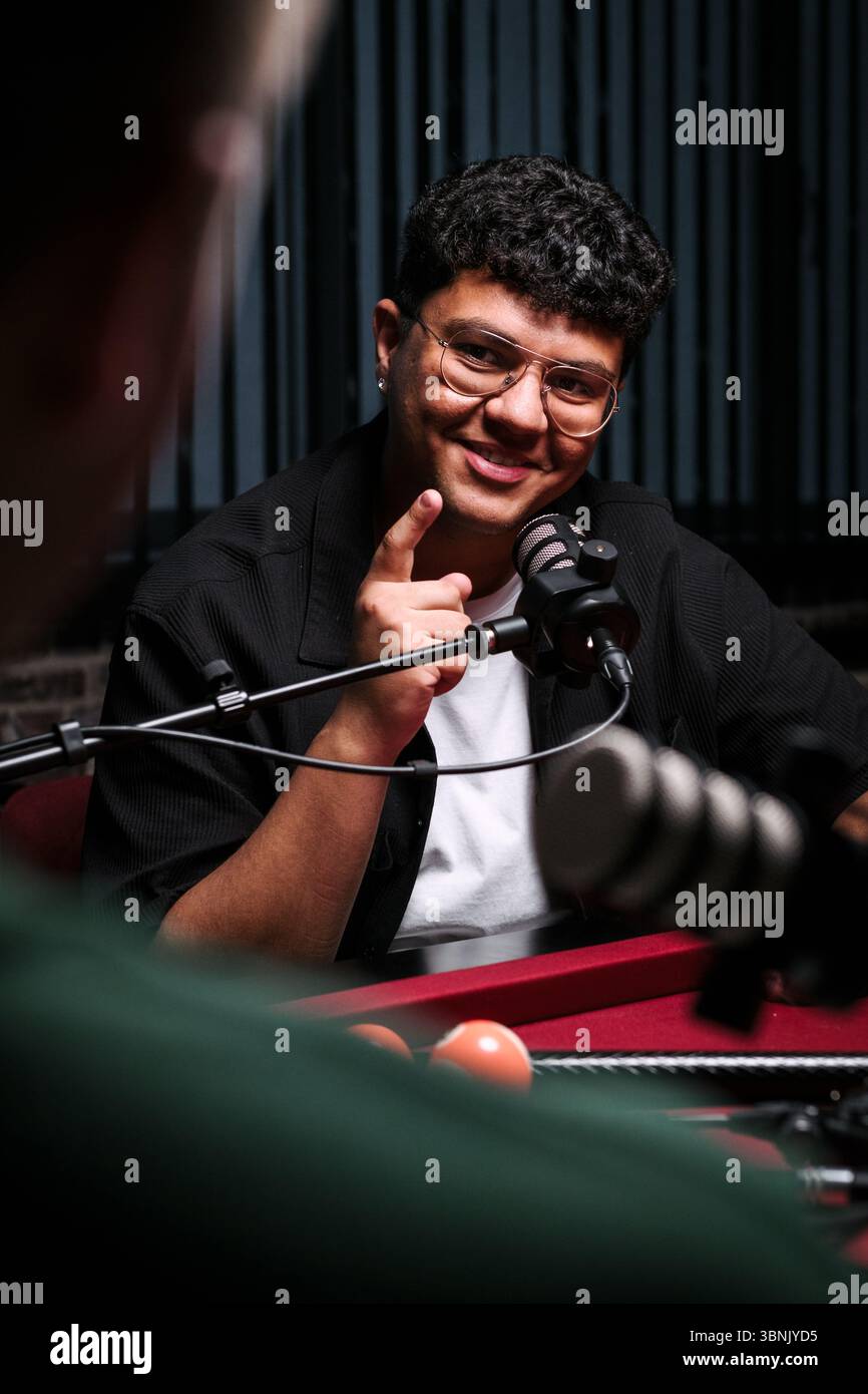 Ein Podcast-Host spricht während einer Live-Aufnahme mit dem Publikum zusammen. Ausgestattet mit professionellen Mikrofonen und einer dynamischen Studioeinstellung, The HOS Stockfoto