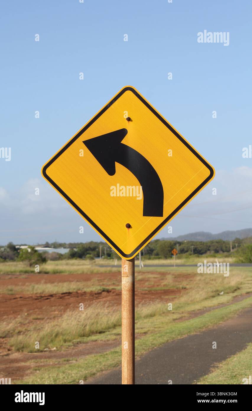 Gelbes Straßenschild mit Linkskurve, das auf einem Metallmast in ländlicher Umgebung angebracht ist Stockfoto