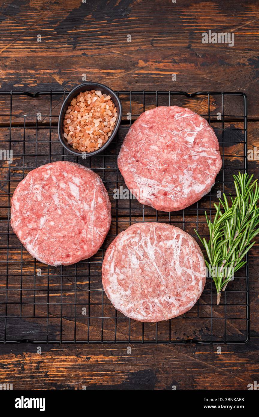 Gefrorene Fleischpasteten, bereit zum Grillen, Forcemeat von Schwein und Rindfleisch für Burger. Hölzerner Hintergrund. Draufsicht Stockfoto