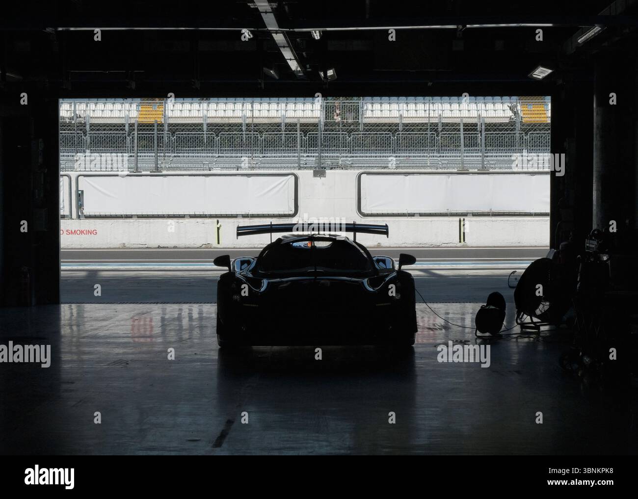 Die Silhouette des Rennwagens in der Boxengasse mit Blick auf die leere Rennstrecke bereitet sich auf ein Motorsport-Event vor Stockfoto