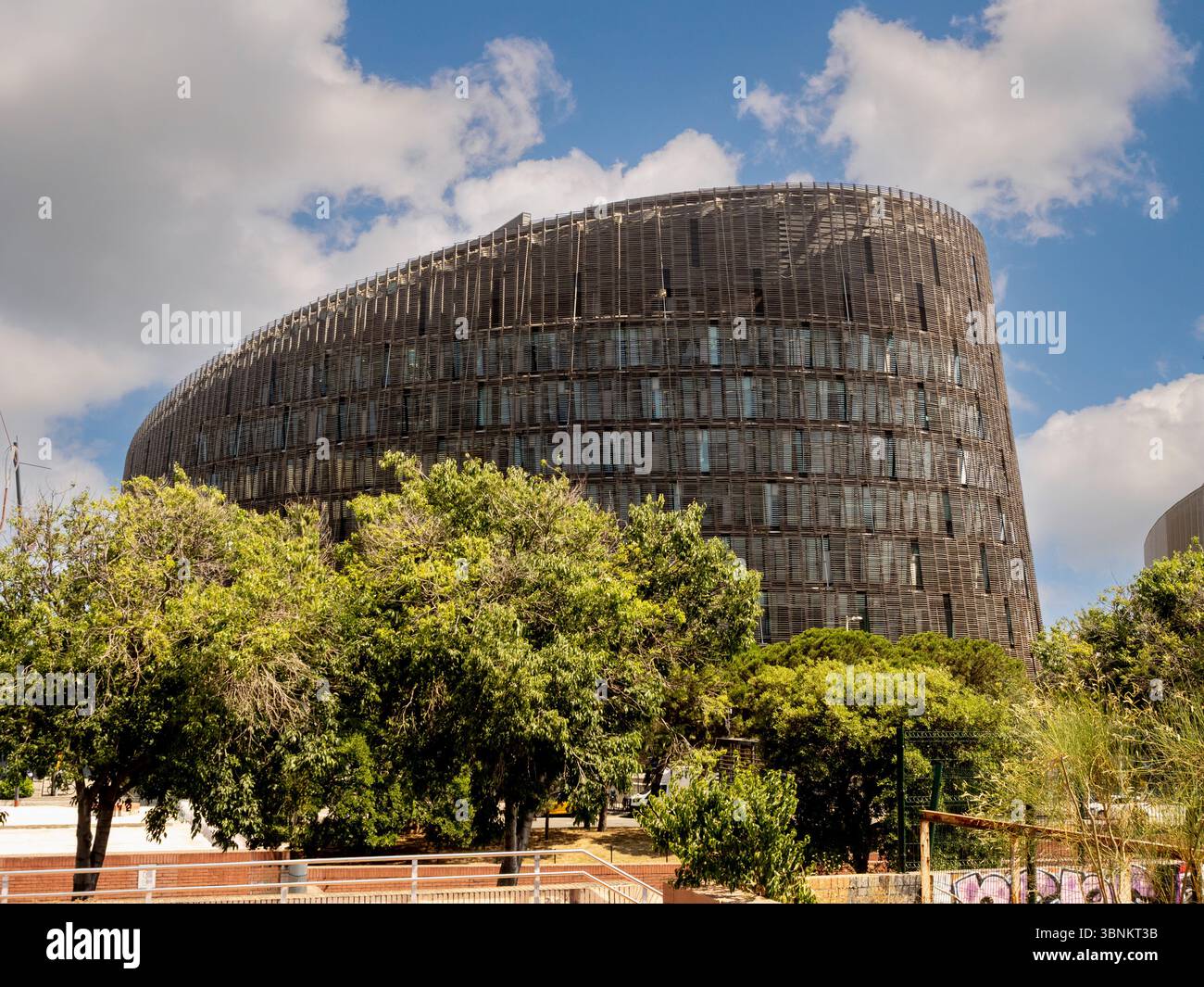 Hinter grünen Bäumen erhebt sich die geschwungene Form des Gebäudes des Biomedical Research Park Barcelona, ein Beispiel für zeitgenössische Architektur. Stockfoto