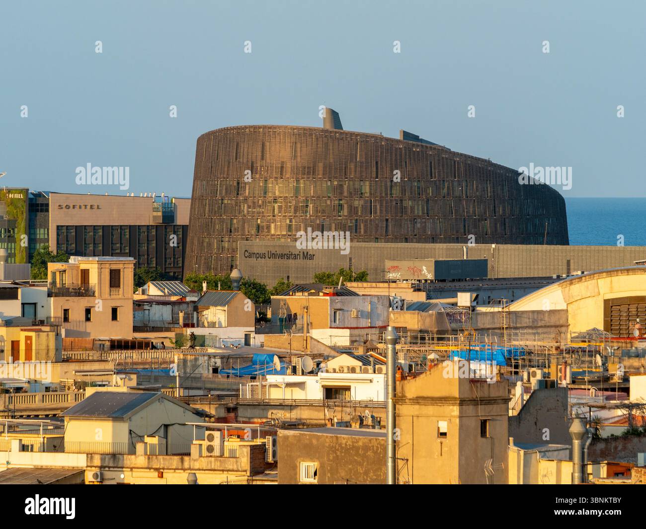 Moderne Architektur des Barcelona Biomedical Research Park (PRBB), der sich über den Dächern der Stadt erhebt, mit dem Mittelmeer im Hintergrund. Stockfoto