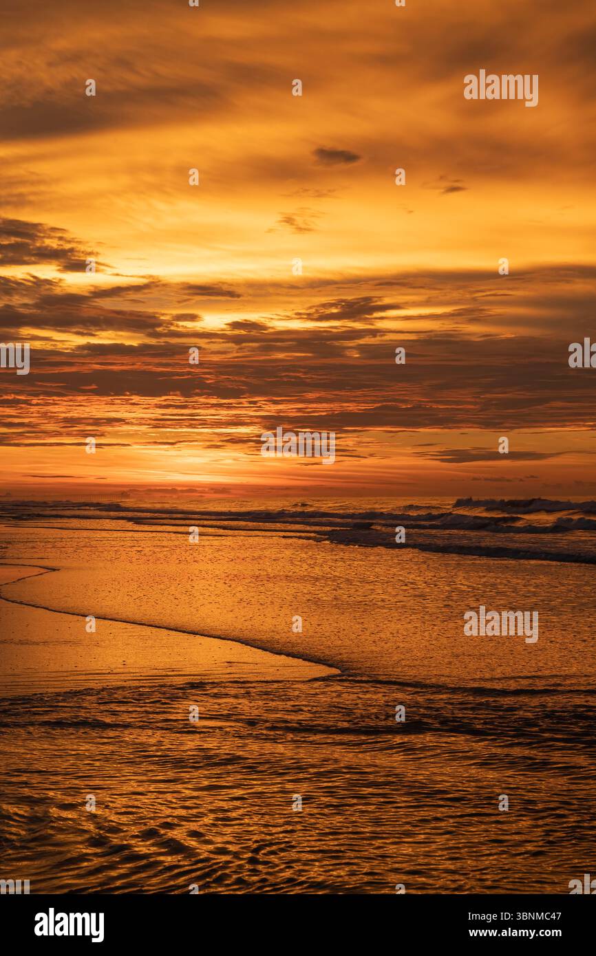 Der helle orangefarbene Himmel in Surise spiegelt sich auf dem Wasser am Strand Stockfoto