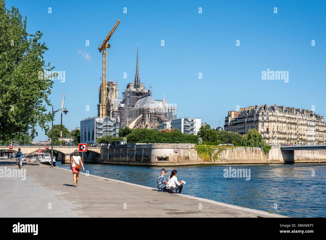 Rückansicht der Kathedrale Notre Dame, die noch 2025 restauriert wurde. Menschen genießen einen warmen Tag entlang der seine mit Notre Dame im Hintergrund Stockfoto