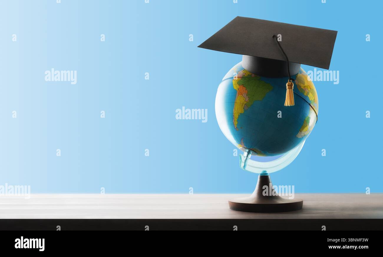 Konzept eines Auslandsstudiums mit einer Kugel auf einem Stand und einer Mörtelplatte darauf auf einem Holztisch und blauem Hintergrund. Vorderansicht. Stockfoto