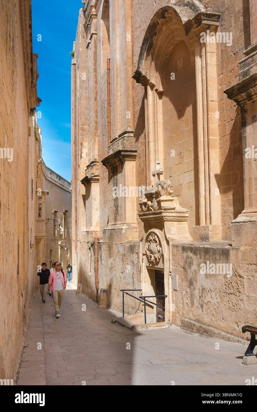 Mann geht auf der Straße, Blick auf einen jungen Mann, der im Sommer allein in einer engen Straße in der historischen ummauerten Stadt Mdina, Malta, läuft. Stockfoto
