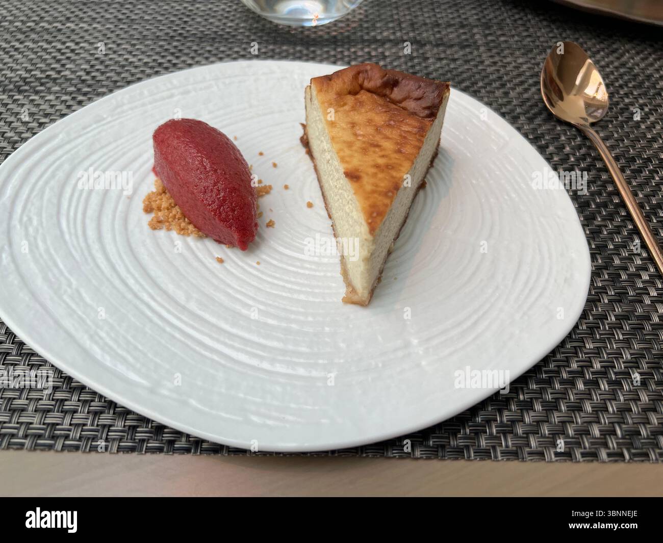Käsekuchen, serviert mit rotem Sorbet und Crumble auf einem weißen Teller. Stockfoto