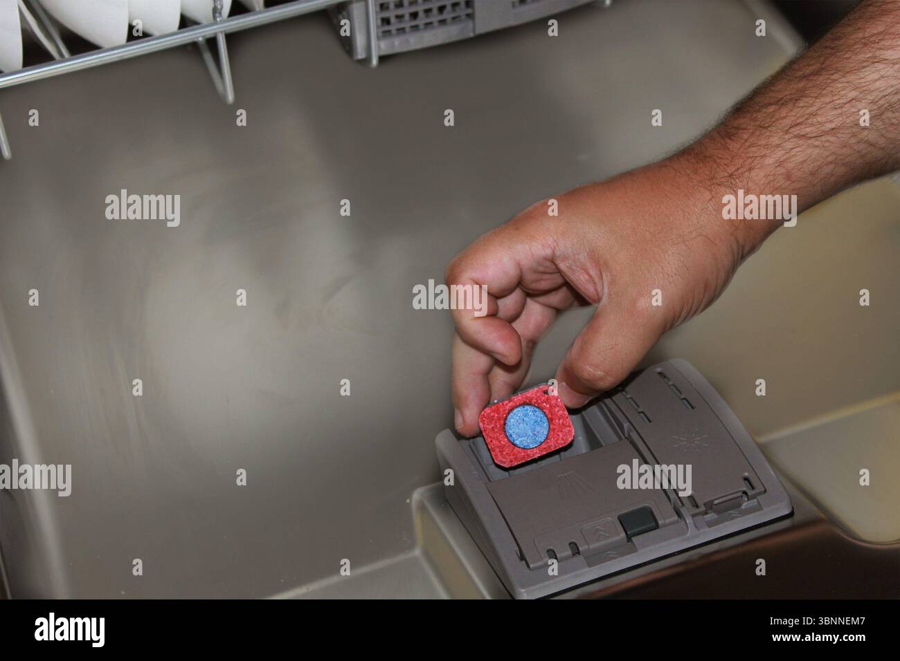 Ein Mann gibt eine Pille in einen Behälter in einen Geschirrspüler. Stockfoto