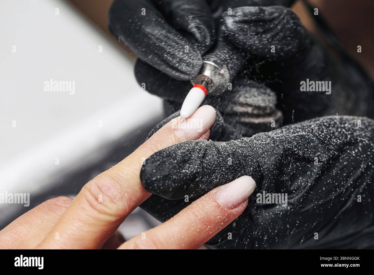 Nageltechniker feilt Fingernägel. Nahaufnahme der Hände in Handschuhen und Kundenhand. Maniküre mit dem elektrischen Nagelwerkzeug. Schönheitsbehandlung im Salon Stockfoto