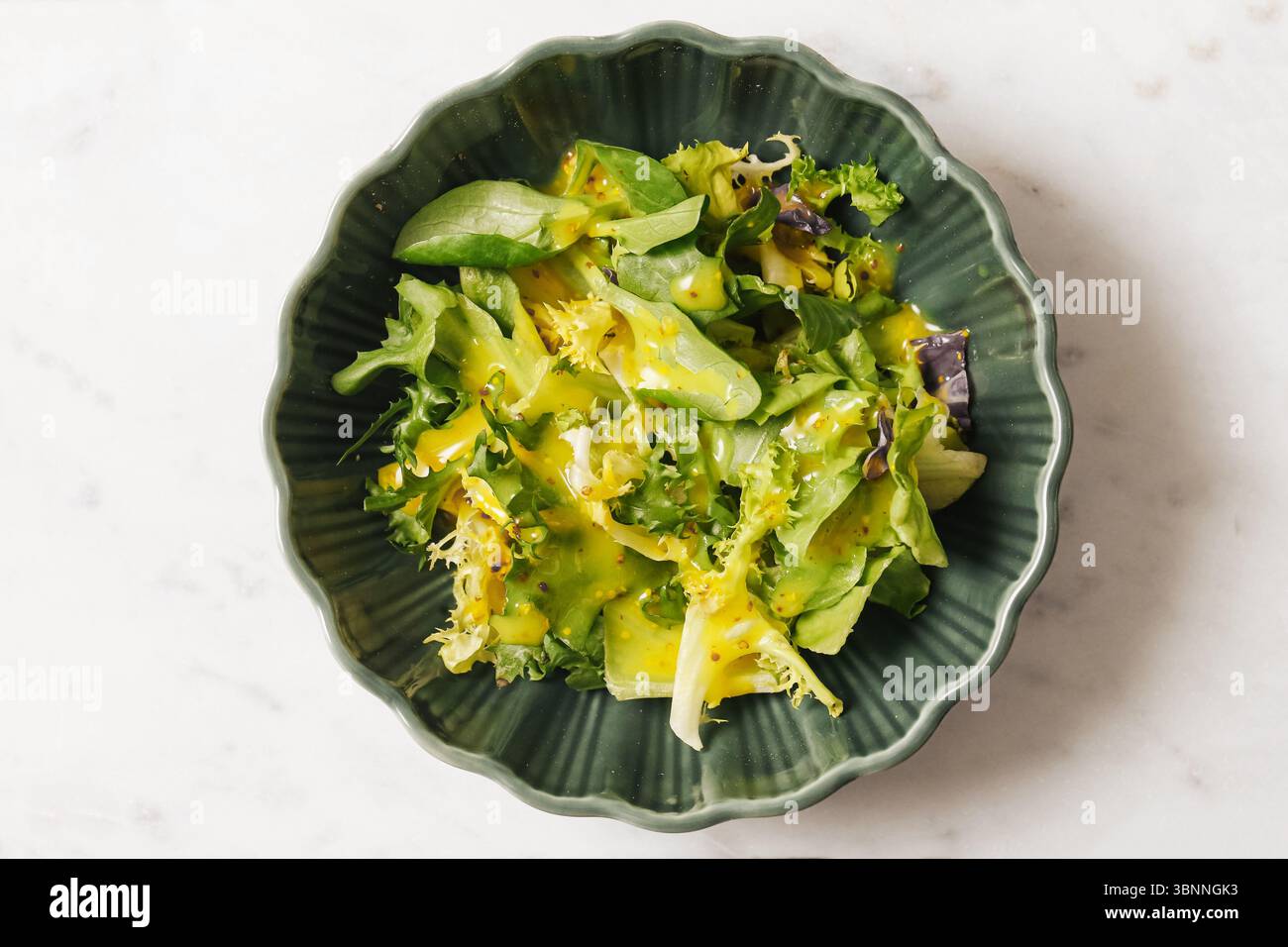 Grüner Blattsalat in Schüssel. Frisches Gemüse mit Dressing. Gesunde vegane Mahlzeit auf Marmorhintergrund. Nahaufnahme von Bio-Lebensmitteln. Knusprige Diät-Textur. Stockfoto