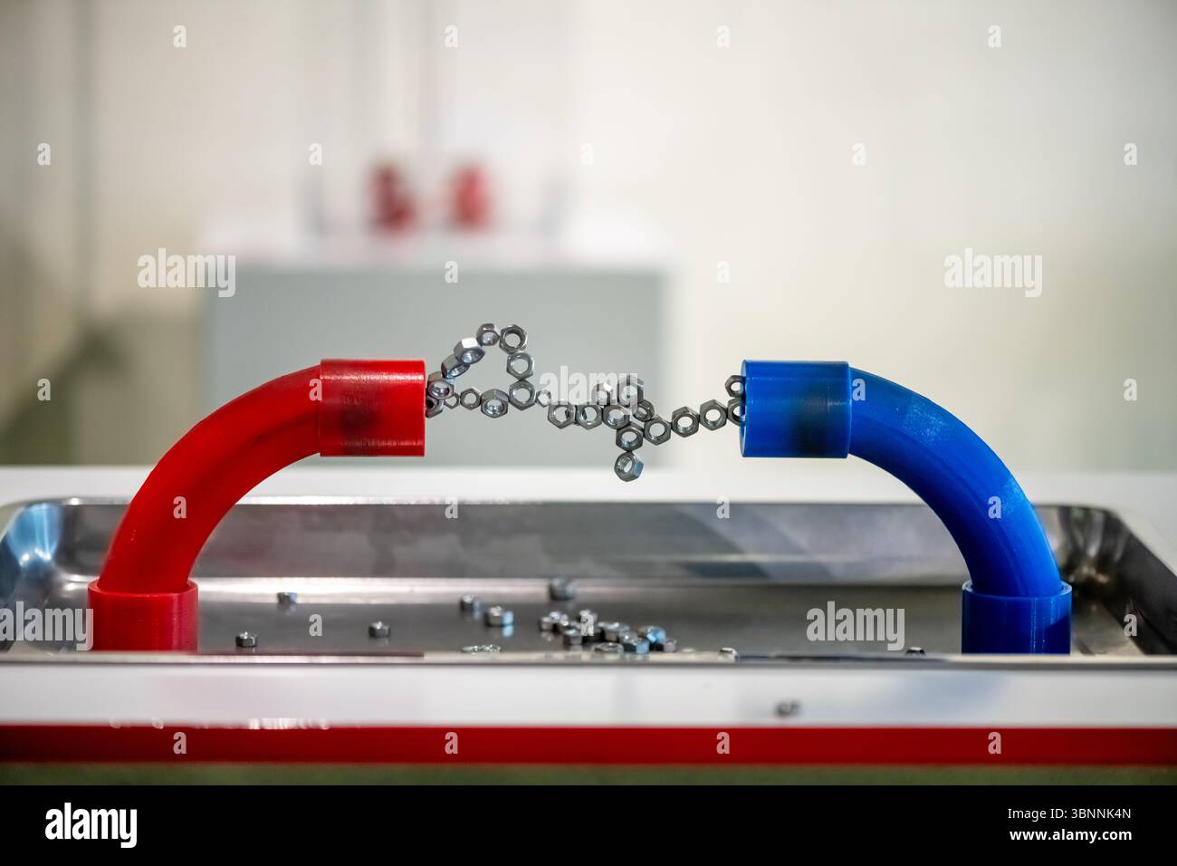 Rote und blaue Magnetrohre ziehen Metallmuttern und -Ketten an und veranschaulichen grundlegende physikalische Konzepte. Das Setup hebt Magnetfelder und Interac hervor Stockfoto