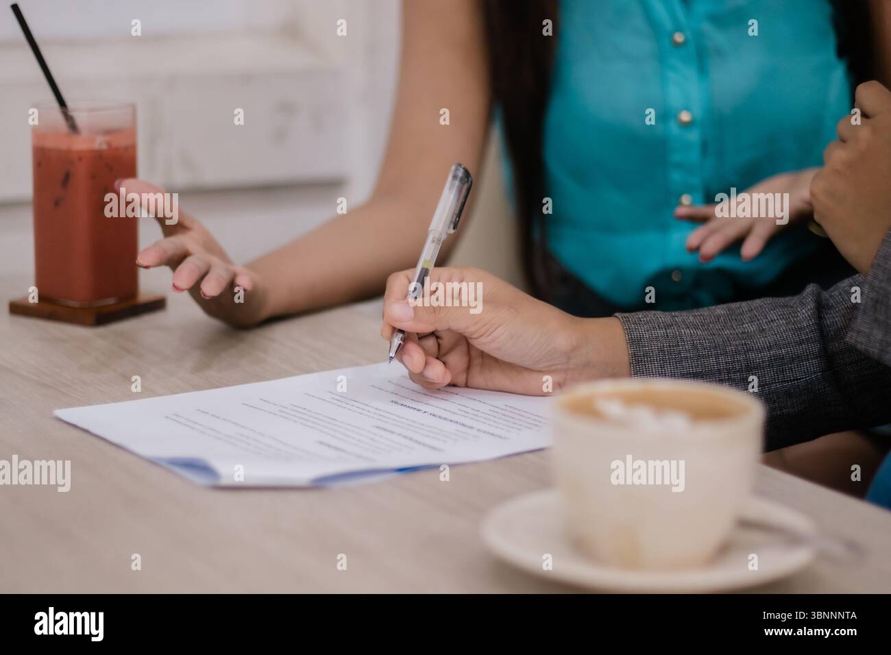 Jemand unterschreibt während des Gesprächs eine Vereinbarung mit Pen. Kaffee und Saft stehen auf dem Tisch. Papierkram und eine professionelle Umgebung stellen Busine dar Stockfoto