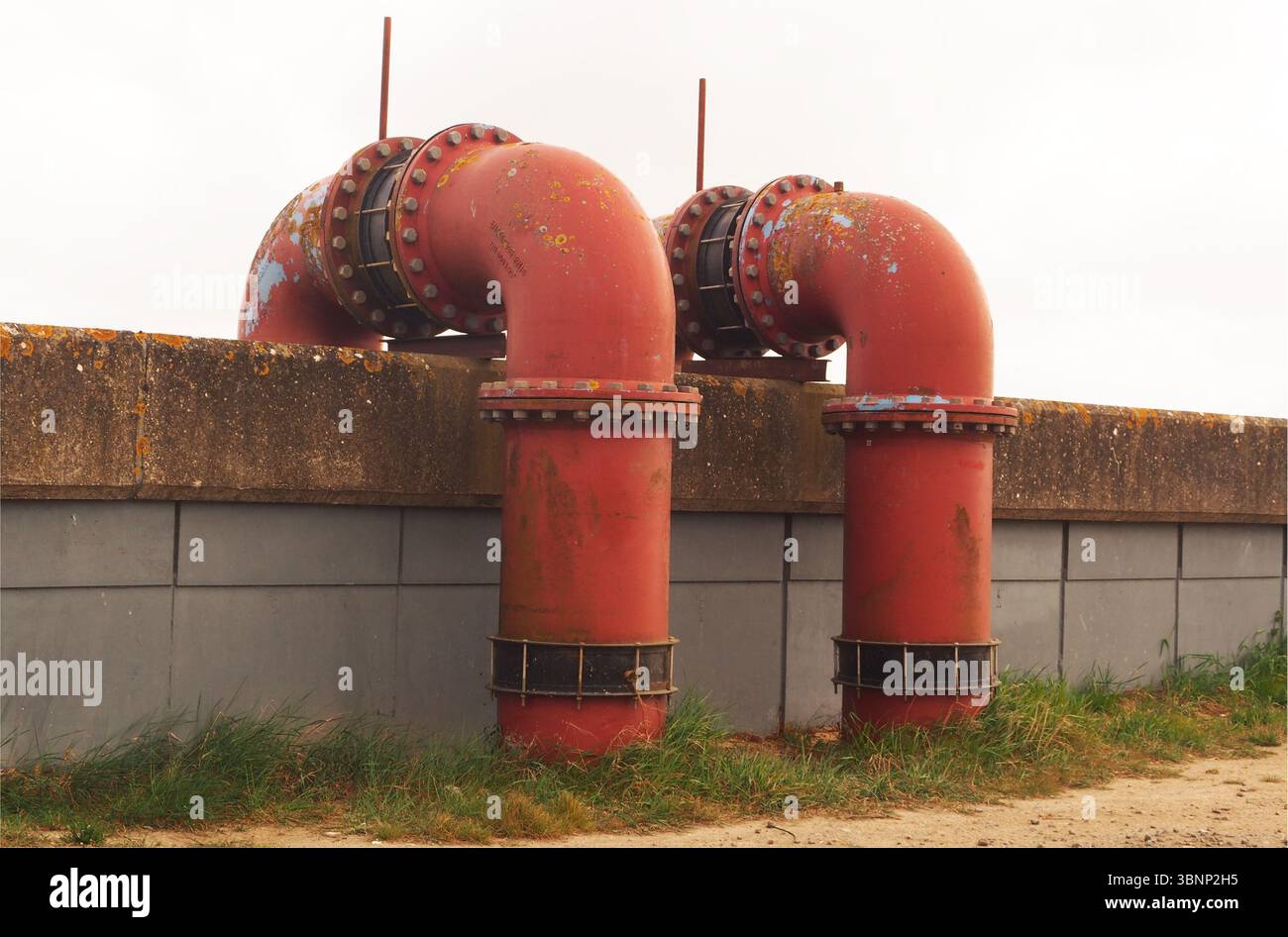 Zwei riesige, rote Schleusenrohre, die über die Mauer bei Breydon Water führen, über die Schleusenebene, nach Breydon Water, Norfolk, England, Großbritannien Stockfoto
