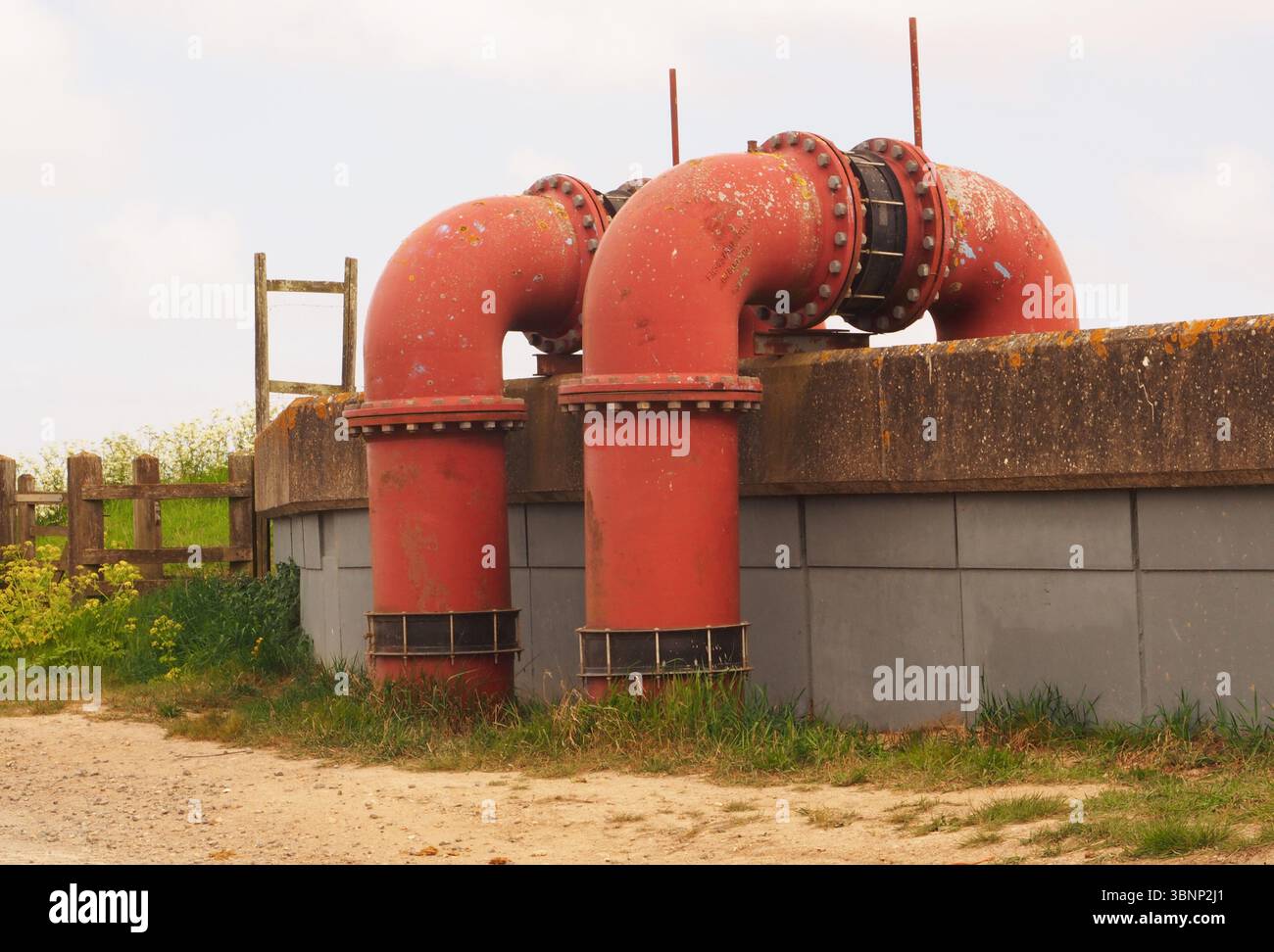 Zwei riesige, rote Schleusenrohre, die über die Mauer bei Breydon Water führen, über die Schleusenebene, nach Breydon Water, Norfolk, England, Großbritannien Stockfoto