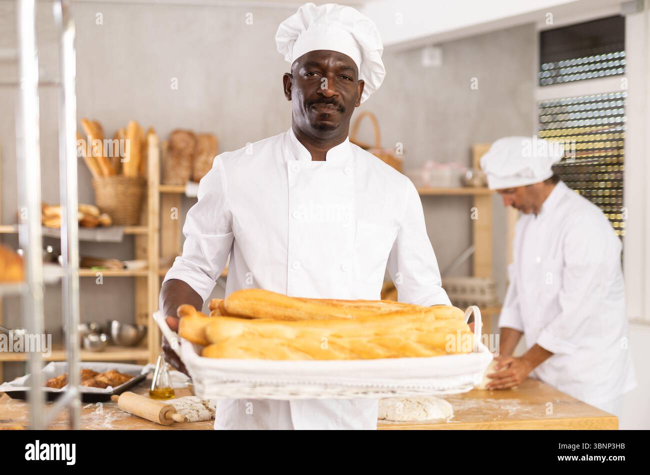 Erfolgreicher afrikanischer Bäcker, der goldene Baguettes in der Bäckerei präsentiert Stockfoto