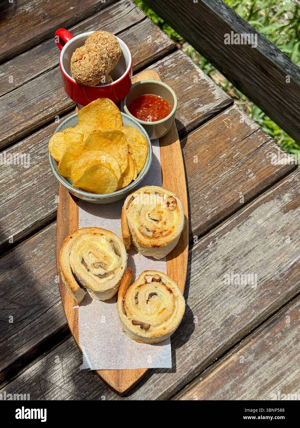 Eine appetitliche Holzplatte mit herzhaften Brötchen, Kartoffelchips, einer Dip-Sauce und einer Krokette, die auf einem rustikalen Holztisch im Freien auf den Azoren serviert wird. Stockfoto