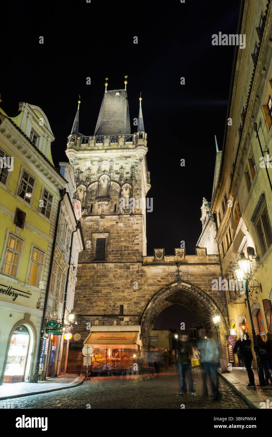 Zeigt einen flachen mittelalterlichen Torbogen in 2D, der über Kopfsteinpflasterstraßen ragt und die Lampe leuchtet auf bewegten Figuren Stockfoto