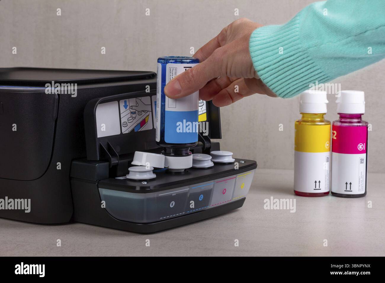 Die Hand einer Frau gießt blaue Farbe aus einer Flasche in den Farbdrucker Stockfoto