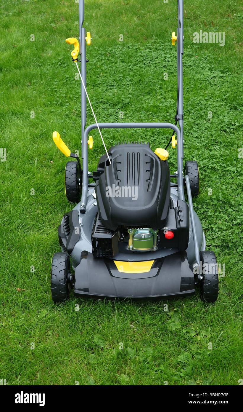 Nagelneuer Rasenmäher im Garten mit langem grünem Gras, bereit für Schneidarbeiten, vertikal Stockfoto