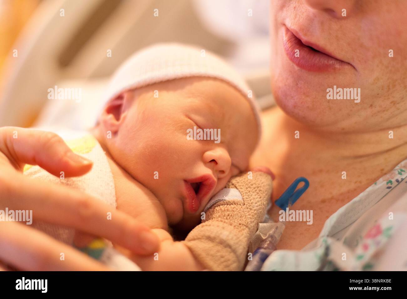 Eine Frau beruhigt ihr neugeborenes Baby, während sie in einem Krankenhausbett auf der Entbindungsstation sitzt. Stockfoto
