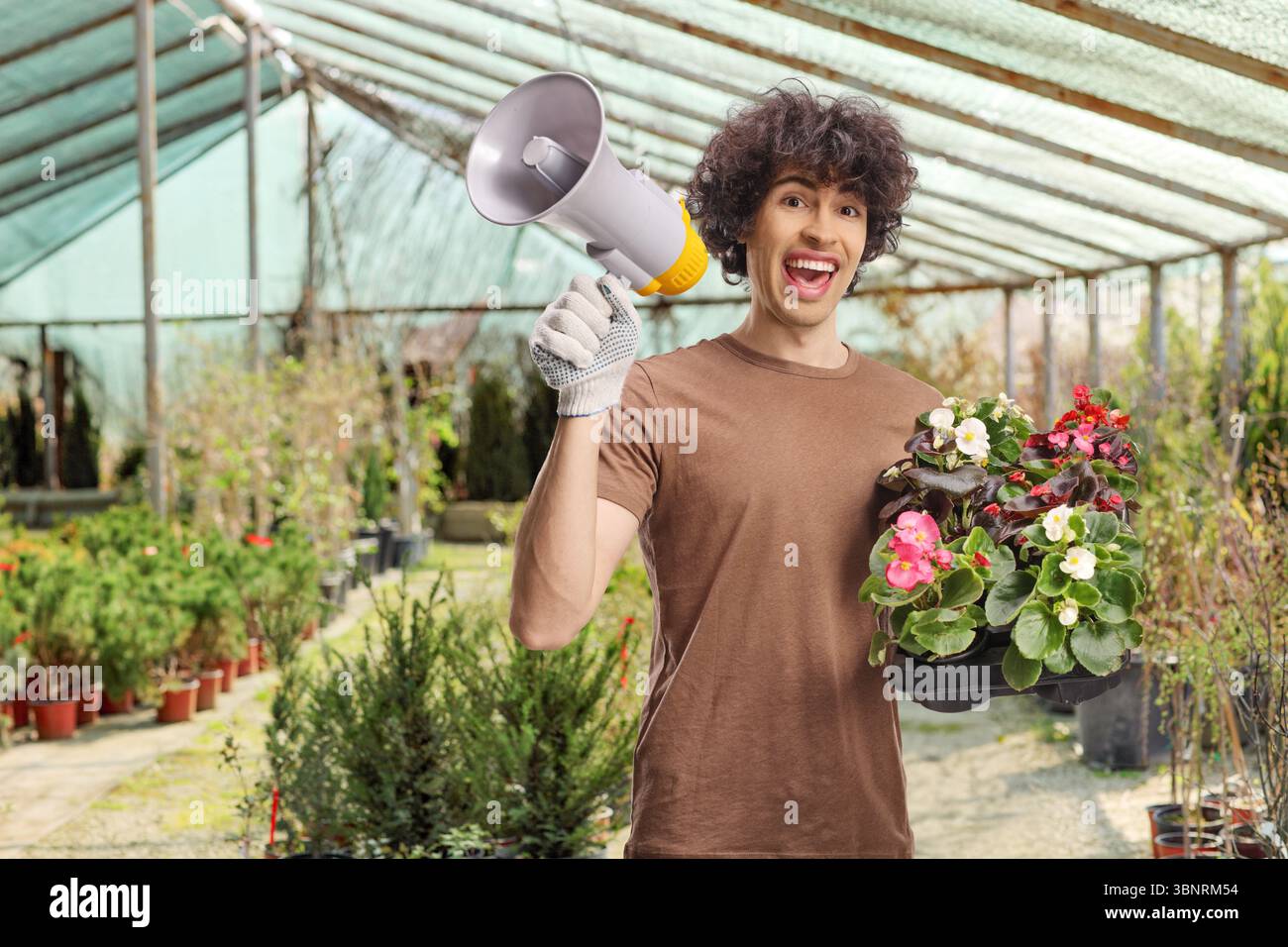 Männlicher Gärtner mit Blumentöpfen und einem Megaphon in einem Gewächshaus Stockfoto