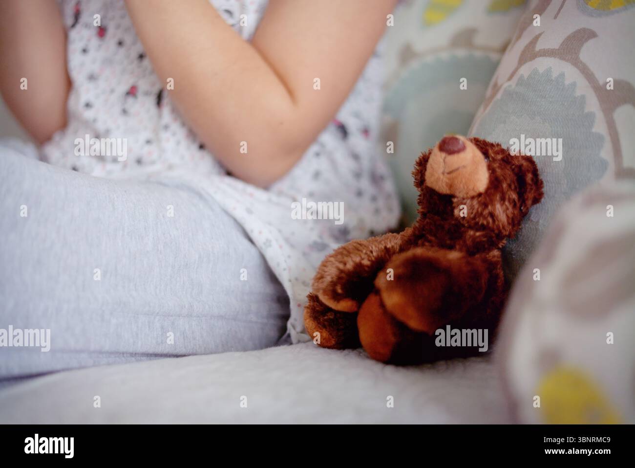 Mädchen mit Down-Syndrom, das mit Teddybär auf dem Sofa sitzt Stockfoto