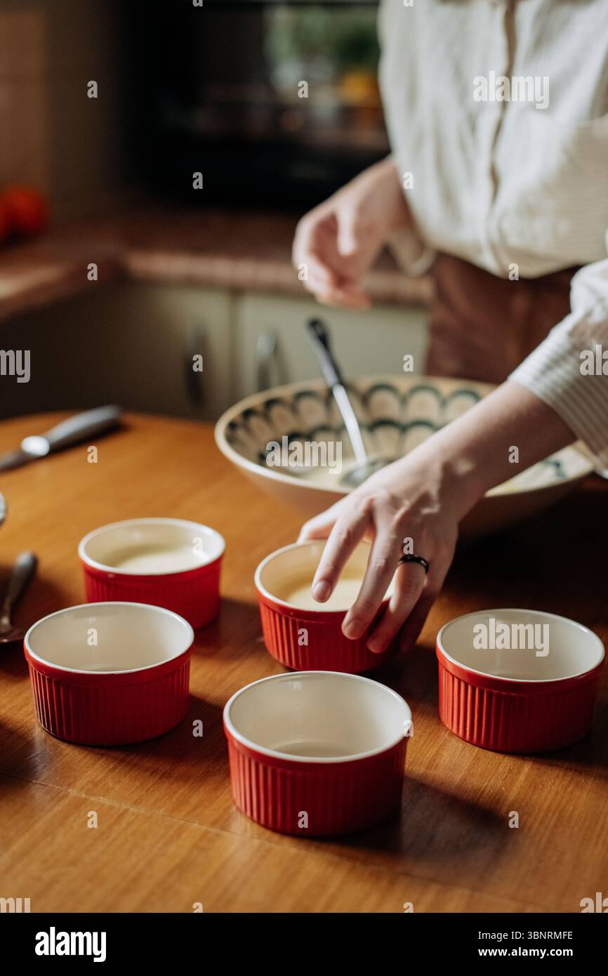 Die junge Frau füllt sorgfältig kleine Keramikramekins mit Crème brûlée Stockfoto