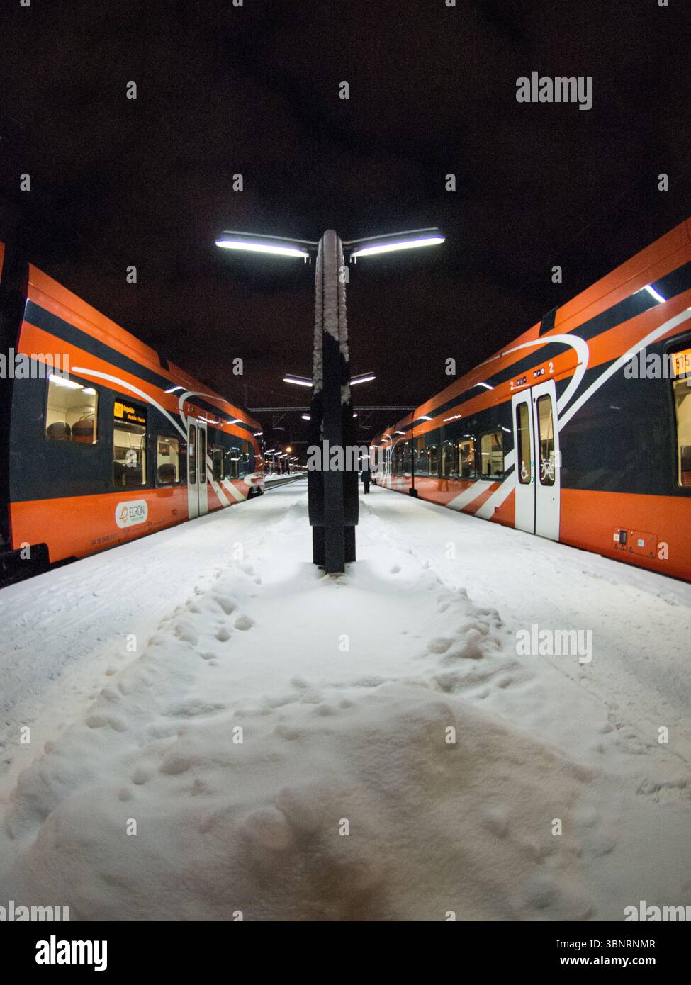 Moderne orangene Personenzüge am verschneiten Bahnsteig in der Nacht, Estland. Stockfoto