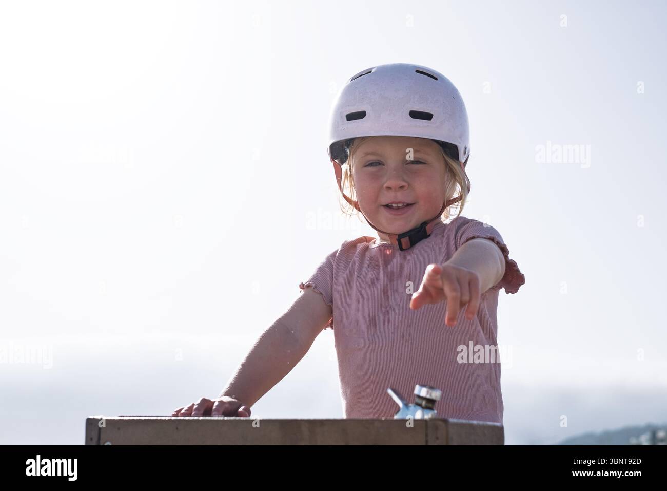 Mädchen in einem Fahrradhelm, das Wasser wegen der Hitze trinkt Stockfoto