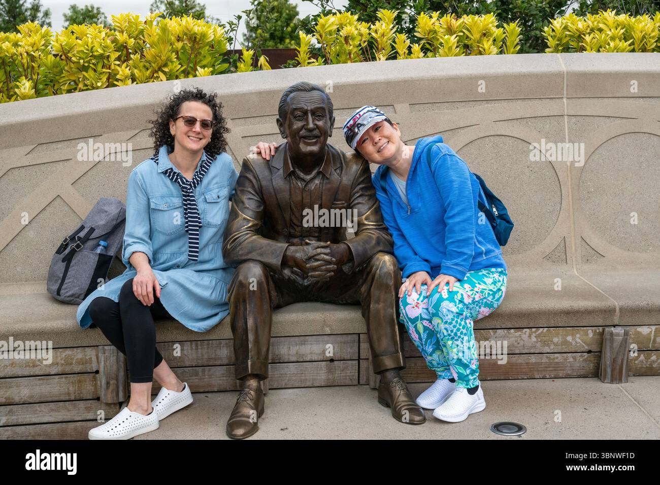 Glückliche Besucher lächeln für die Kamera, während sie neben einer Bronzestatue von Walt Disney am Eingang von EPCOT sitzen. Stockfoto