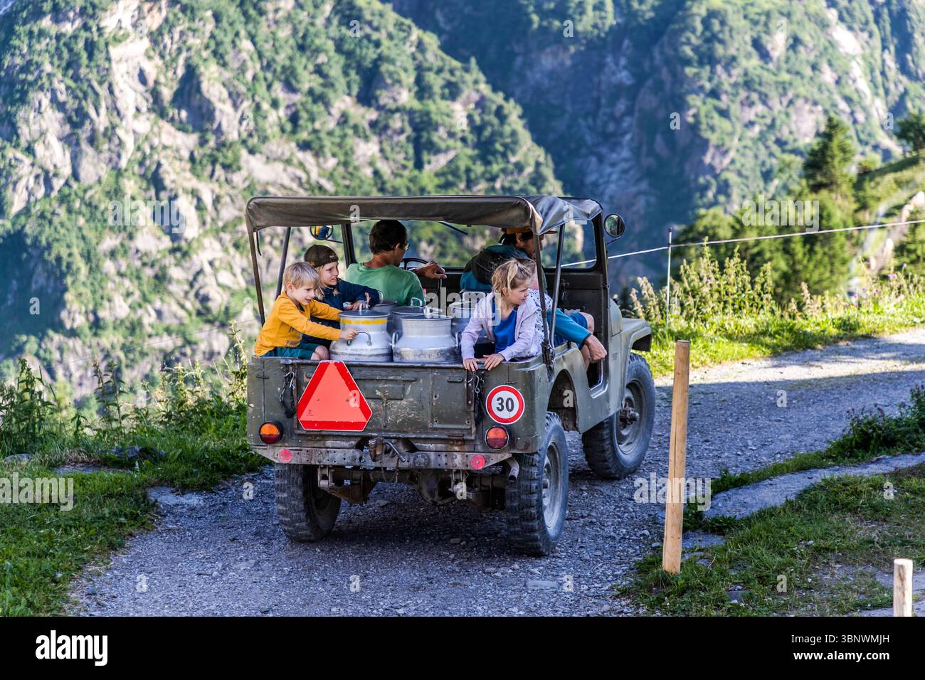 Ruedi Zurfluh bringt Gastkinder zur nahegelegenen Almkäserei und liefert Milch, Hobiel Alp, Engelbergtal am Surenenpass. Urlaub auf dem Bauernhof. Fahren in einem Geländefahrzeug mit Milchkannen auf einer Schotterpiste in den Bergen. Die Szene spielt in Attinghausen, Kanton URI, Schweiz, und zeigt den Transport von Milch von einer Alm Stockfoto