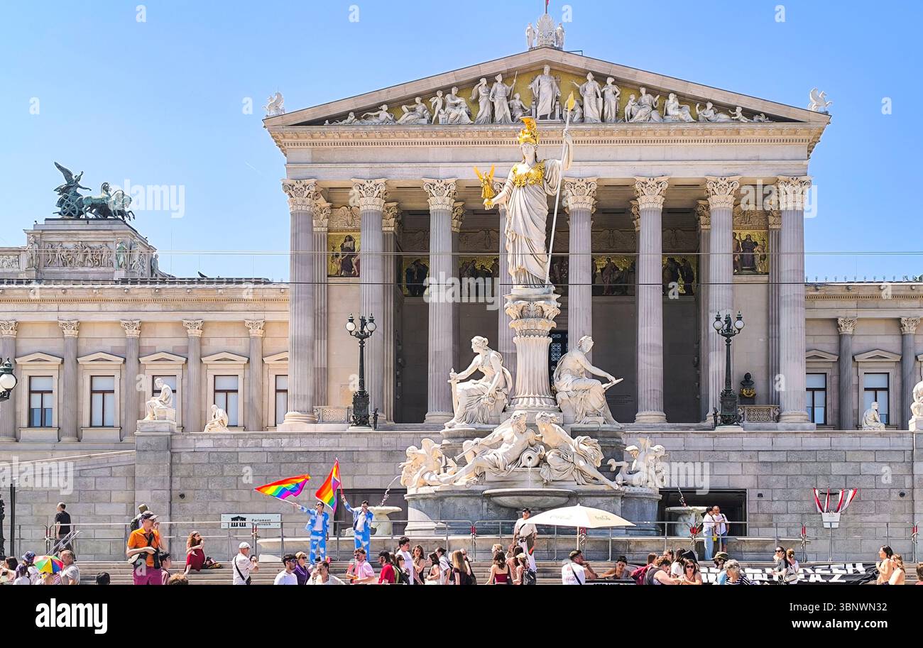Wien, Österreich, 06.14.2025: Zwei Männer in blauen Anzügen schwenken LGBTQ-Fahnen vor dem österreichischen Parlamentsgebäude während des Pride Day marsches an sonnigem Tag Stockfoto