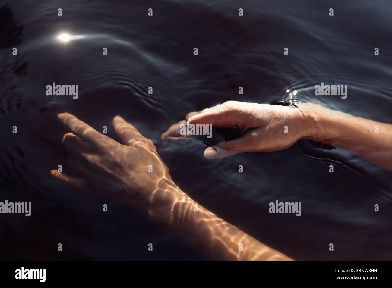 Die Finger berühren smaragdgrüne Gewässer und erzeugen sanfte Wellen, während das Sonnenlicht auf der Oberfläche tanzt, was dem friedlichen geldautomaten am See einen ruhigen Touch verleiht Stockfoto