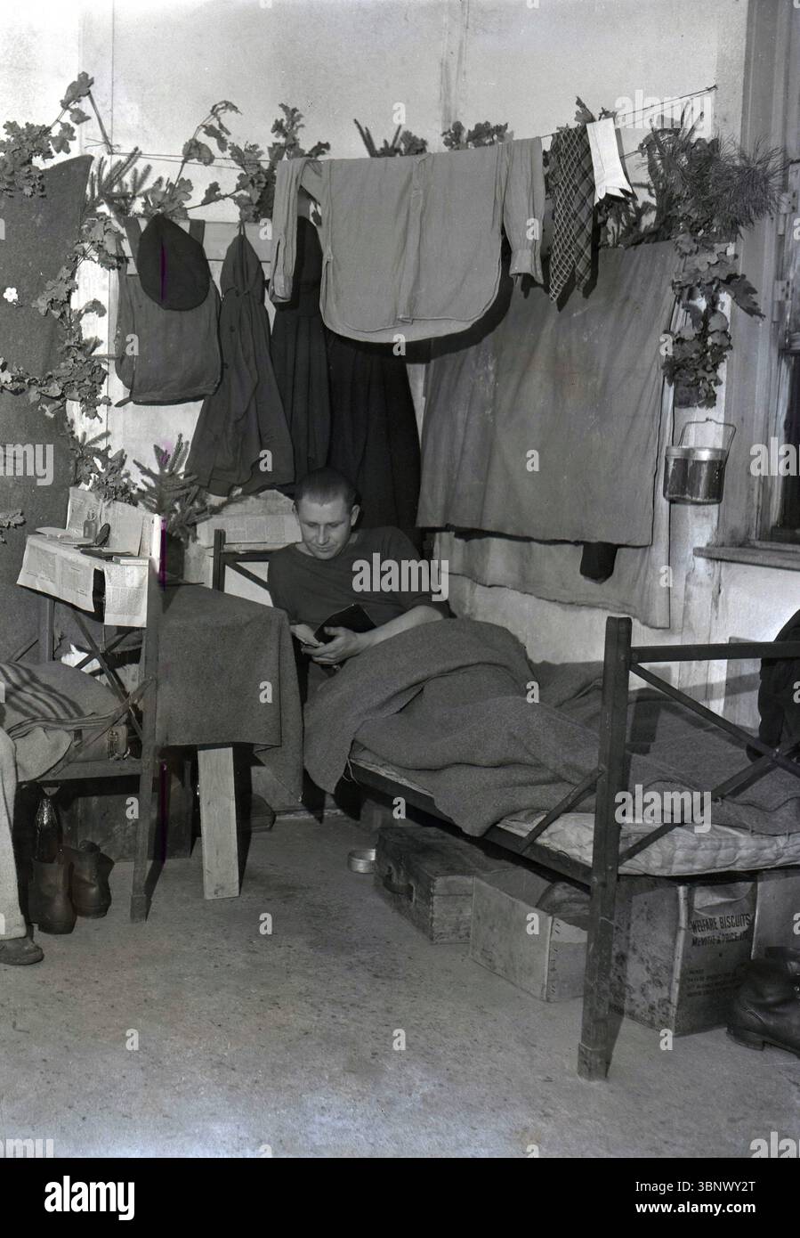 1946, historisch, ein ausländischer Arbeiter in seinem Bett im Volkswagen-Werk Wolfsburg, möglicherweise ein junger lettischer Mann. Hemd und Socken hängen an einer Wäscheleine. Kiste Sozialkekse, McVitie & Price Ltd. Unter dem Bett. Unter der Kontrolle der britischen Armee begann ab Juni 1945 die Produktion von Volkswagen-Autos, und viele Flüchtlinge und Migranten kamen aus den ehemaligen deutschen Gebieten in Osteuropa nach Wolfsburg, um Nahrung, Wohnung und Arbeit zu suchen. Stockfoto