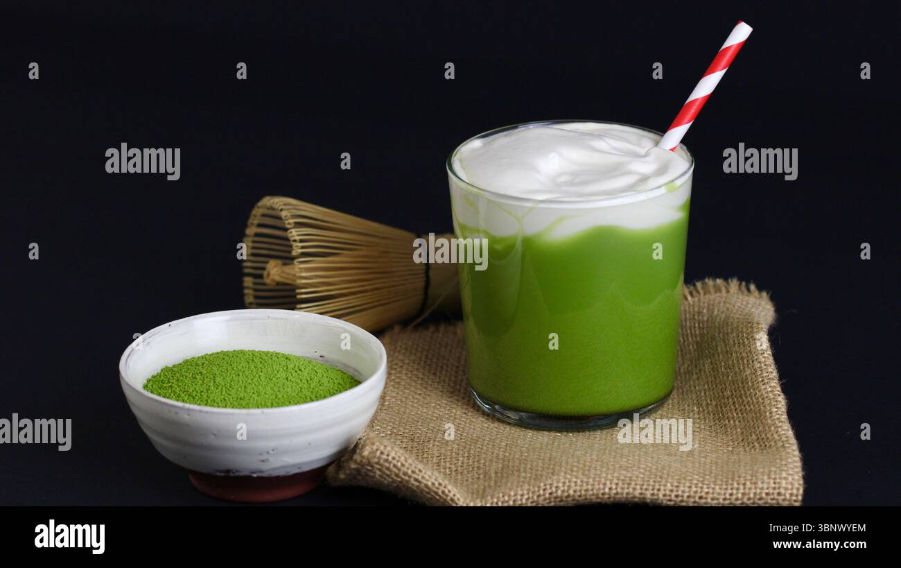 Iced Matcha Latte mit cremigem Schaum und rotem Strohhalm auf dunklem Hintergrund - japanische Tee-Ästhetik Stockfoto