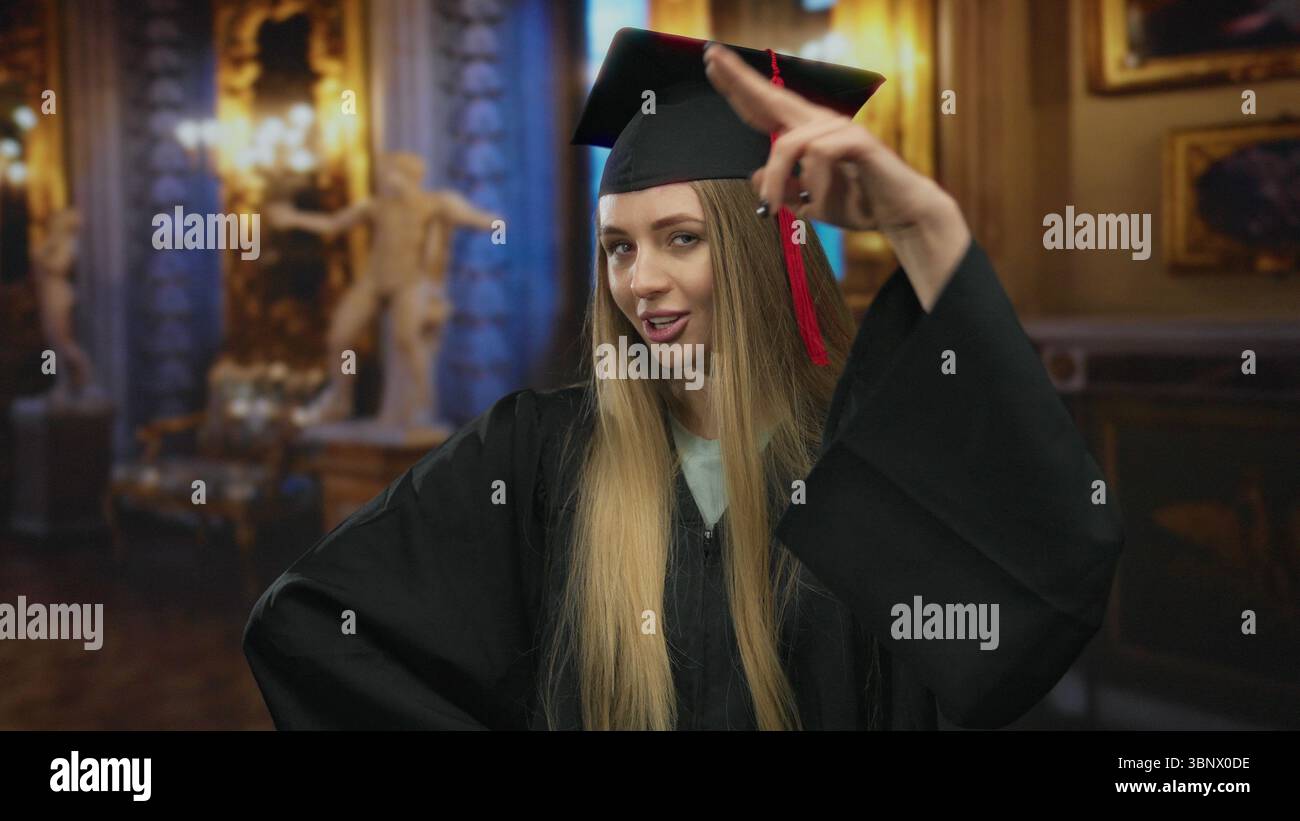 Die junge Frau im Abschlusskleid posiert selbstbewusst in einem eleganten Museum, das Kunst- und Kulturhighlights zeigt. Stockfoto