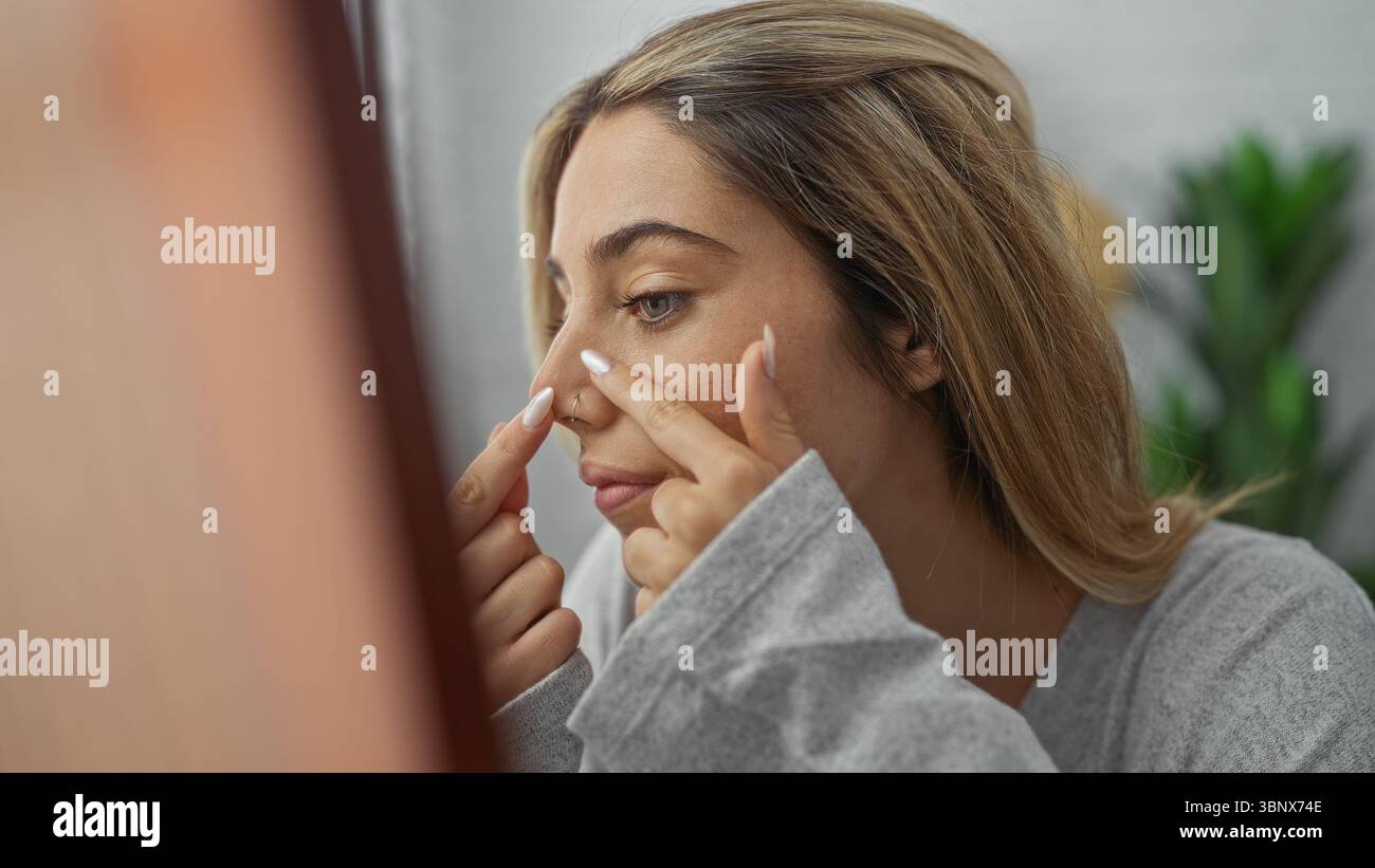 Frau drinnen entfernt Unreinheiten von der Nase in einem hellen Wohnzimmer, die sich auf die Hautpflege konzentriert, mit lässiger Kleidung und natürlichem Licht, die ihre Schönheit verbessern Stockfoto