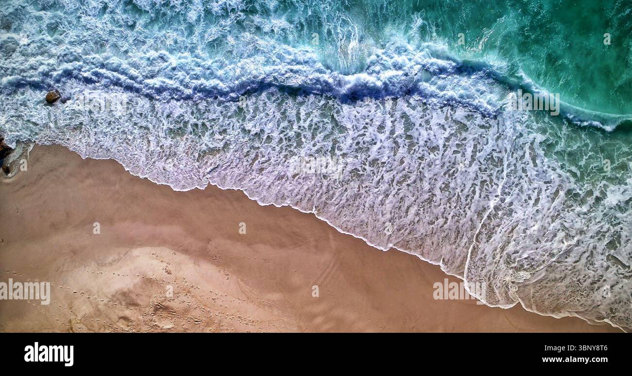 Türkisfarbene Meereswellen stürzen auf glatten, braunen Sand und bilden weißen Schaum in flachem Design Stockfoto