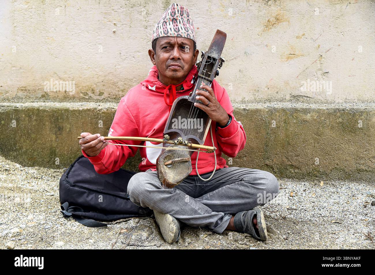 Ein erfahrener Musiker sitzt auf dem Boden und spielt anmutig ein traditionelles Streichinstrument wie Sitar oder Veena während einer Übungseinheit. Stockfoto