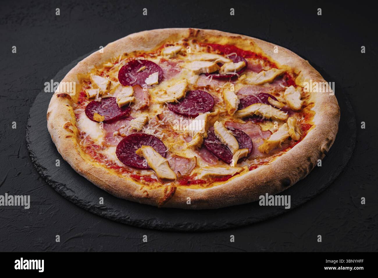 Stillleben, Peperoni Pizza mit Basilikum und Parmesan auf schwarzem Steinteller Stockfoto