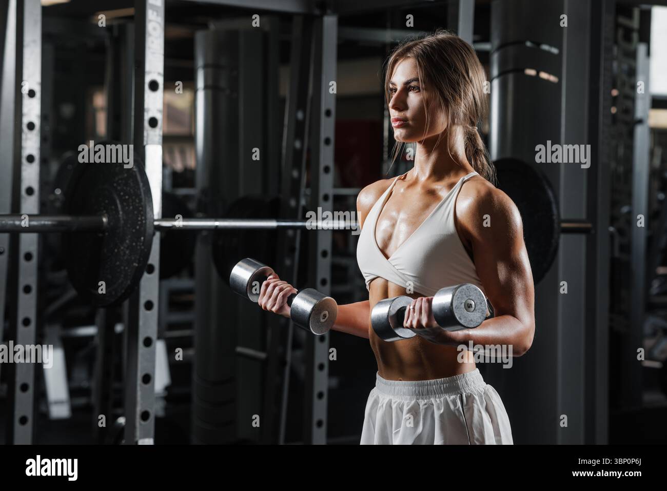 Selbstbewusste athletische Frau Heben Kurzhanteln im Fitnessstudio Kraft Workout starke Arme Fitness Motivation und gesunde Lebensweise Stockfoto