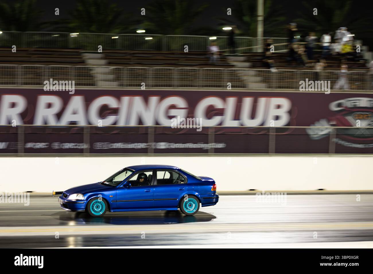 Motion Blur Drag Racing bei Nacht, bei dem Autos auf der Rennstrecke mit Zuschauern in der Nähe konkurrieren Stockfoto