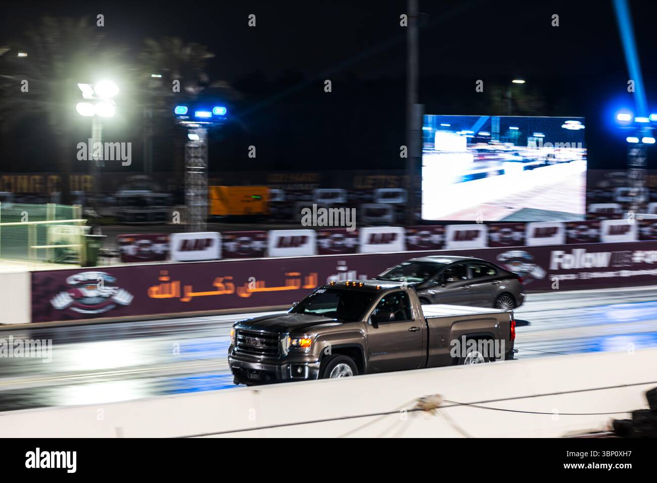 Motion Blur Drag Racing bei Nacht, bei dem Autos auf der Rennstrecke mit Zuschauern in der Nähe konkurrieren Stockfoto