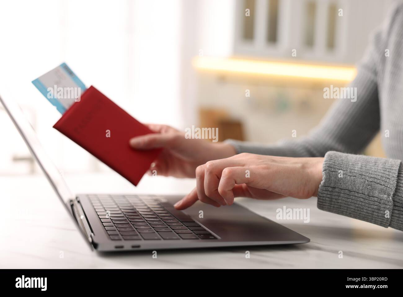 Frau mit Reisepass und Flugticket mit Laptop an weißem Marmortisch drinnen, Nahaufnahme Stockfoto