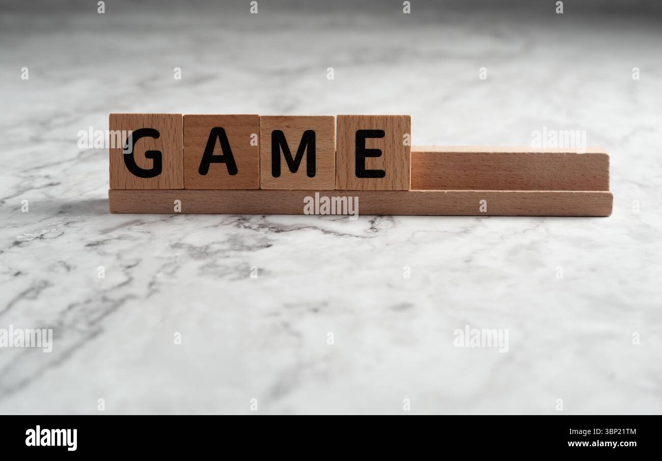 Das Wort „SPIEL“ wurde mit hölzernen Buchstabenblöcken formuliert, die auf einem Holzgestell aufgestellt waren, isoliert vor einem hellen, strukturierten Hintergrund Stockfoto