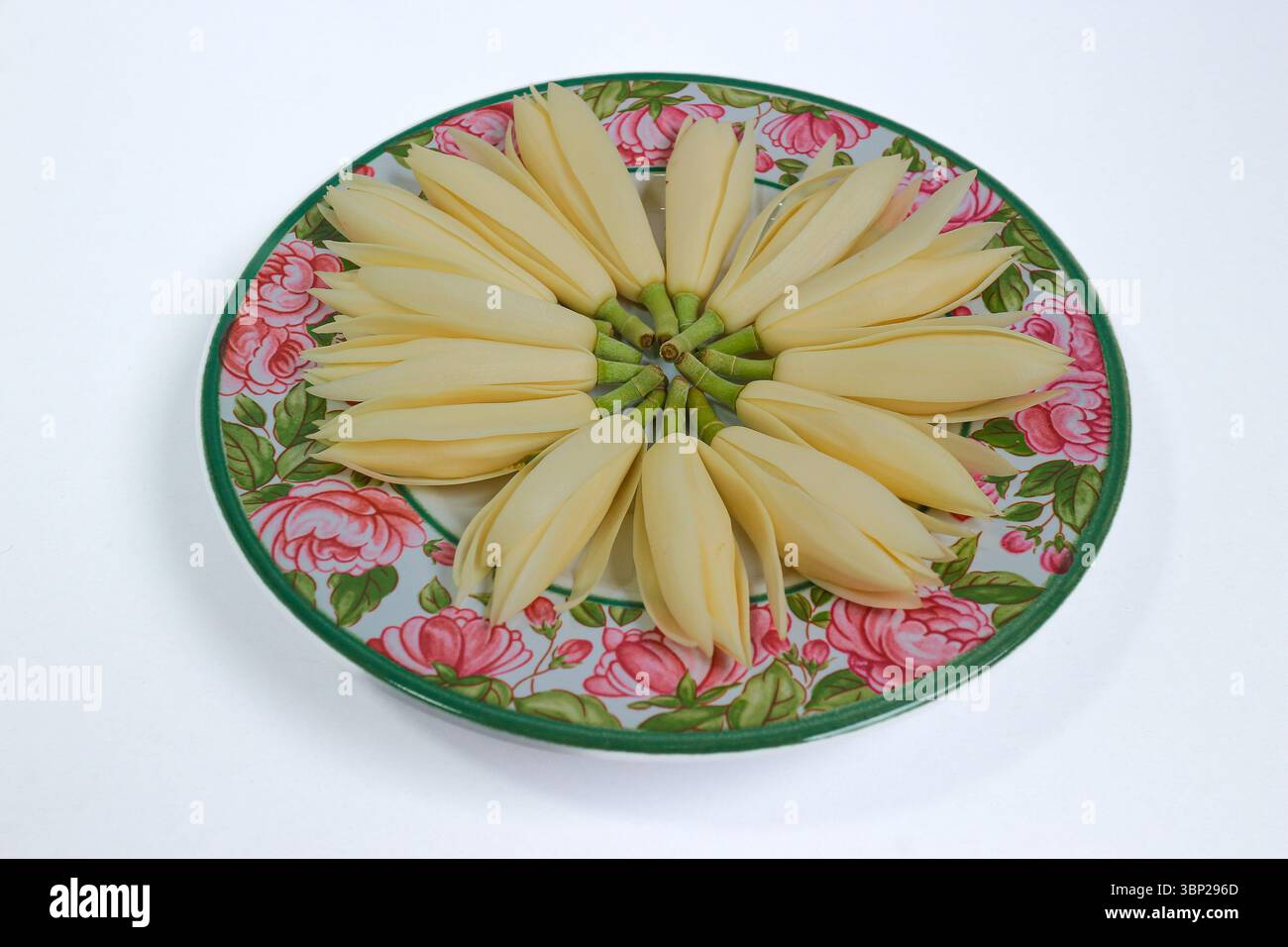 Duftende weiße Champakblüten im Kreis auf Vintage-Keramikplatte mit rosafarbenem Blumenmuster. Spa-Stil, elegante und natürliche ruhige Stimmung. Stockfoto