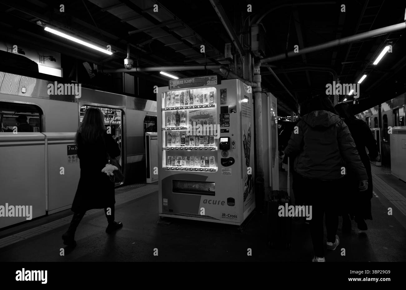 Schwarzweißfoto eines Bahnsteigs mit einem leuchtenden Verkaufsautomaten Stockfoto