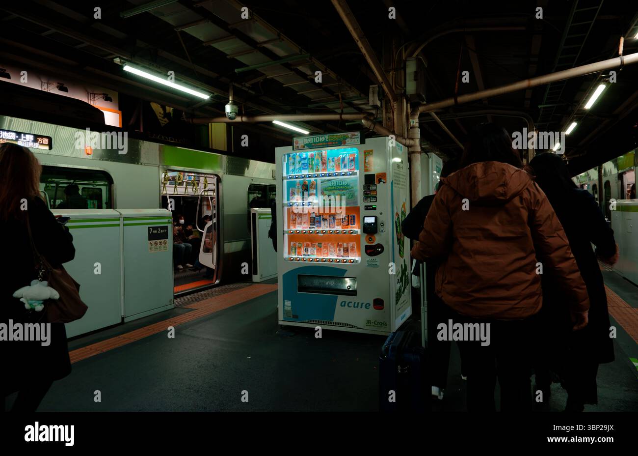 Der Bahnsteig mit Fahrgästen, Verkaufsautomaten und Zugtüren der Yamanote-Linie öffnen sich unter Leuchtstofflampen Stockfoto