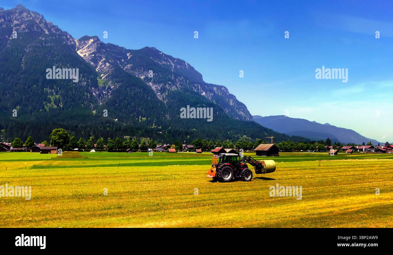 Ein roter Traktor pflügt an einem sonnigen Tag ein landwirtschaftliches Feld vor dem Hintergrund von Wäldern und Bergen. Stockfoto