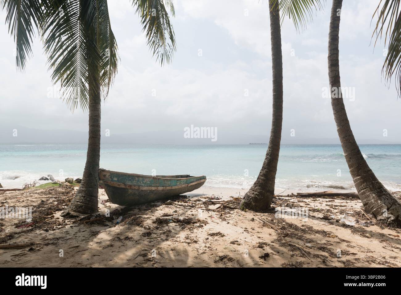 Kleines Holzboot am Strand zwischen Palmen, Insel in der Ferne. San Blas Archipel, Panama. Stockfoto